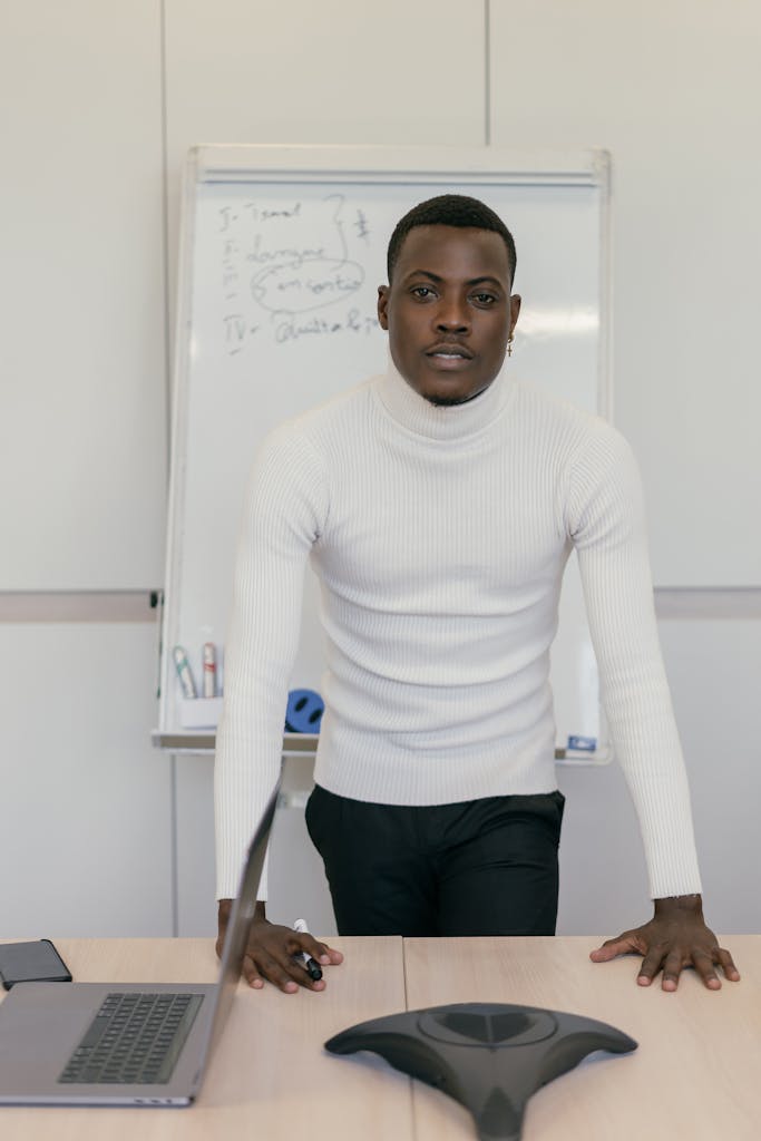 A confident businessman in a white turtleneck presenting in a modern office setting.